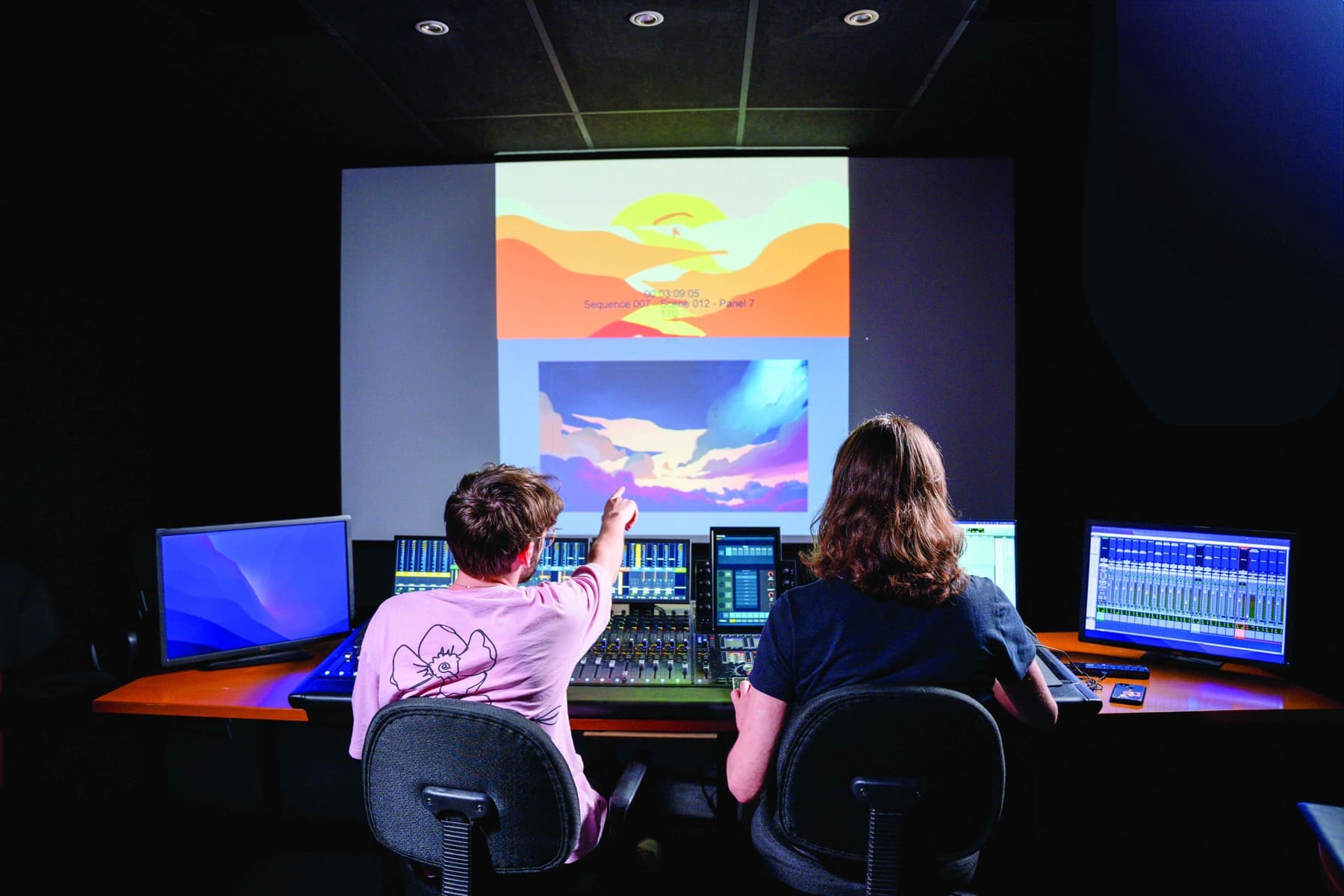 Deux étudiants de l'ESRA en studio de post-production, devant une console de mixage et des écrans de montage.