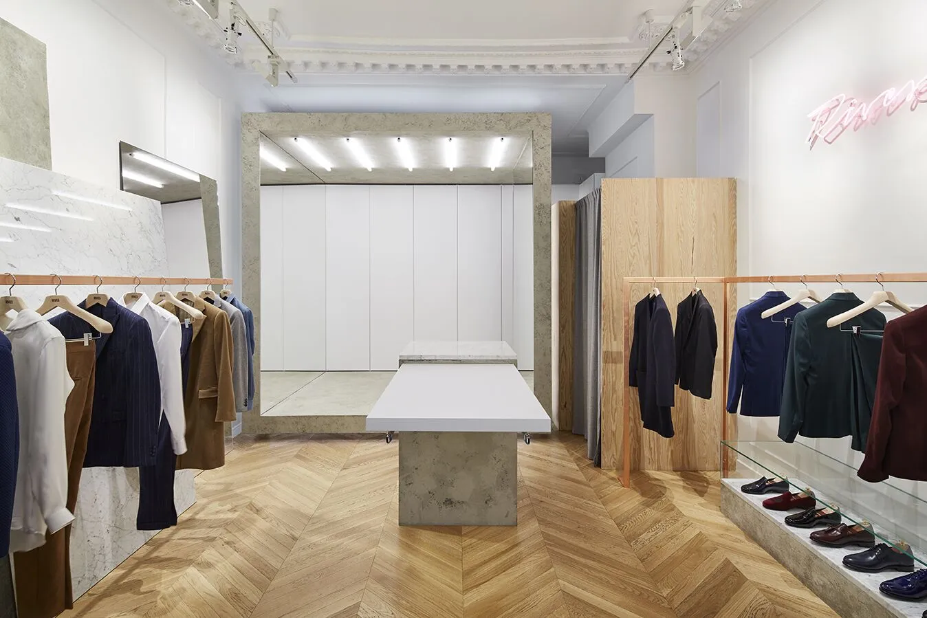 Boutique RIVES Paris, atelier de tailleur sur-mesure pour homme : parquet à chevrons, marbre et portants de costumes. Client accompagné par l'agence GEO PeakView AI.